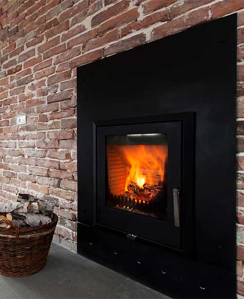 Wood Burning Insert in older brick wall.  Basket of wood sitting to the left.