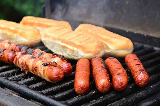 Hotdogs and buns on the grill.  Some of the hot dogs are wrapped in bacon and look yummy.