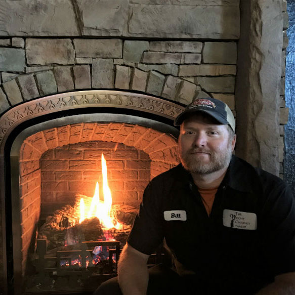 Bill Hartshorn in front of fireplace wearing logo shirt and hat in front of keystone fireplace